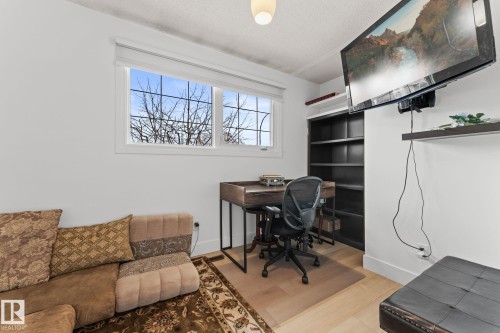 Hardwood-style flooring extends throughout this room, featuring a built-in shelving unit, a mounted television, and a window with white trim - 16424 106 Street, Edmonton, AB - Indoor
