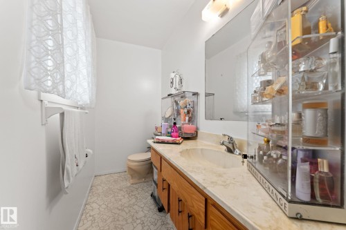 Bathroom featuring a light-toned vanity with an integrated sink, wood cabinetry, and a large wall-mounted mirror - 16424 106 Street, Edmonton, AB - Indoor Photo Showing Bathroom