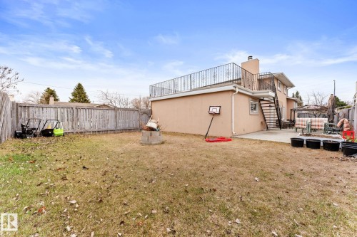 Expansive fenced backyard featuring a concrete patio, a built-in fire pit, and a balcony with wrought iron railing - 16424 106 Street, Edmonton, AB - Outdoor