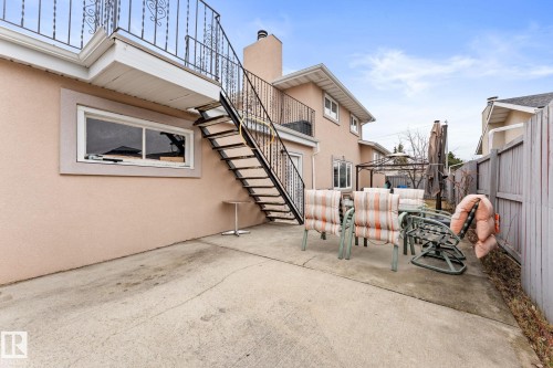 Concrete patio featuring a stucco exterior, black metal staircase, and an upper-level balcony with decorative railing - 16424 106 Street, Edmonton, AB - Outdoor