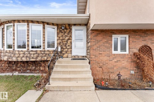 Stone and brick exterior featuring a multi-pane bay window, concrete entry steps with a black metal handrail, white entry door, and an exterior wall lantern - 16424 106 Street, Edmonton, AB - Outdoor
