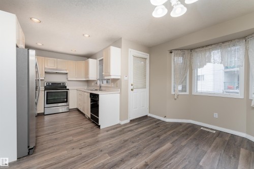 The kitchen features a stainless steel refrigerator and range, light-toned cabinetry, and recessed lighting - 3 9703 174 Street, Edmonton, AB - Indoor Photo Showing Kitchen