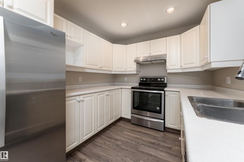 The kitchen features a stainless steel refrigerator, stainless steel range with overhead ventilation, white cabinetry, and light-colored countertops - 3 9703 174 Street, Edmonton, AB - Indoor Photo Showing Kitchen With Double Sink