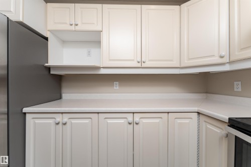 The kitchen features light-colored cabinetry, a coordinating countertop, and a stainless steel refrigerator - 3 9703 174 Street, Edmonton, AB - Indoor