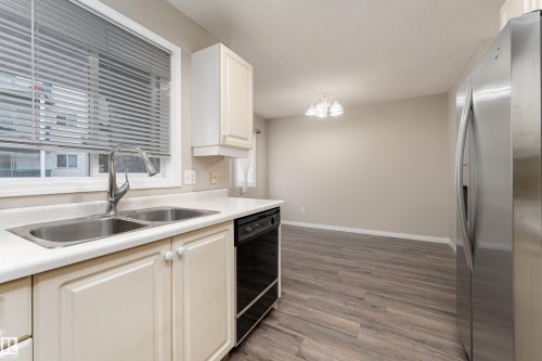 The kitchen features a double basin stainless steel sink with a gooseneck faucet, light-colored cabinetry, and a window with blinds - 3 9703 174 Street, Edmonton, AB - Indoor Photo Showing Kitchen With Double Sink