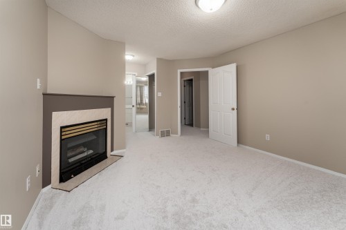 The property features a room with light-colored carpeting, a fireplace with a tiled surround, and neutral-toned walls - 3 9703 174 Street, Edmonton, AB - Indoor With Fireplace