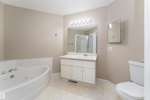 This bathroom features a corner soaking tub, a vanity with a white countertop and basin sink, a wall-mounted mirror with vanity lighting, and a separate shower enclosure - 3 9703 174 Street, Edmonton, AB - Indoor Photo Showing Bathroom