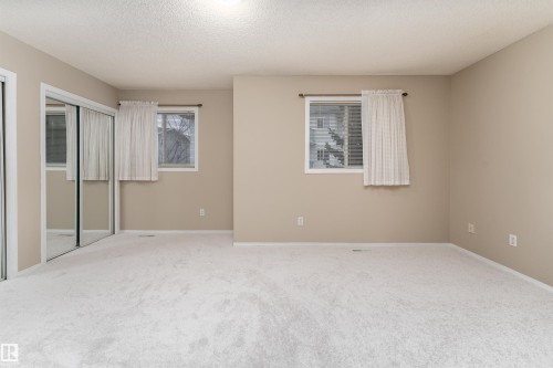 This room features light-colored carpeting, two windows with curtains, and a mirrored sliding closet door - 3 9703 174 Street, Edmonton, AB - Indoor Photo Showing Other Room