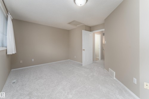 This interior space features light-colored carpeting, neutral-toned walls, and a window with blinds providing natural light - 3 9703 174 Street, Edmonton, AB - Indoor Photo Showing Other Room