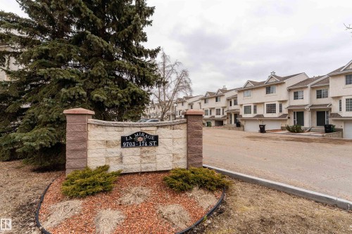 The property features a stone and brick entrance sign, surrounded by mature evergreens and landscaping - 3 9703 174 Street, Edmonton, AB - Outdoor