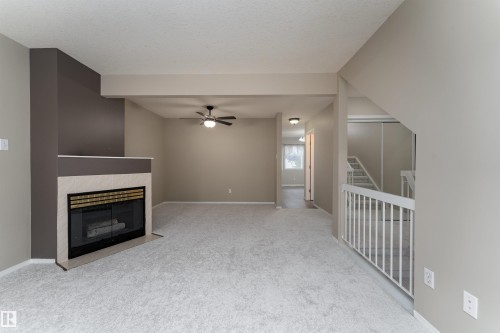Living area featuring light-colored carpeting, a fireplace with a tiled surround, and a ceiling fan - 3 9703 174 Street, Edmonton, AB - Indoor With Fireplace