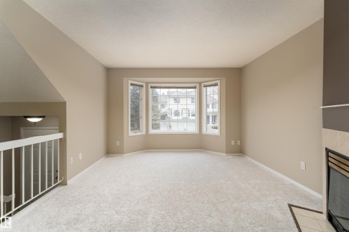 Living area featuring light colored carpet, a bay window, and a corner fireplace with a tiled surround - 3 9703 174 Street, Edmonton, AB - Indoor Photo Showing Other Room
