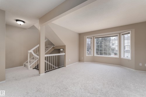 Living area with light-colored carpeting, a bay window providing exterior views, and a staircase with white railings - 3 9703 174 Street, Edmonton, AB - Indoor
