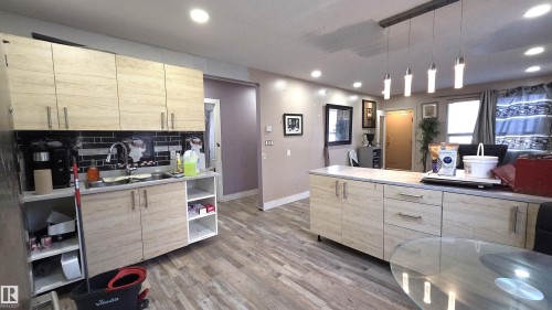 Open-concept kitchen featuring wood-finish cabinetry, black subway tile backsplash, recessed lighting, and a modern linear pendant fixture - 10644 96 Street, Edmonton, AB - Indoor Photo Showing Kitchen