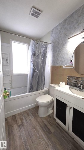 Bathroom featuring wood-finish flooring, a white vanity with under-sink storage, a circular mirror, and a tub with an integrated shower - 10644 96 Street, Edmonton, AB - Indoor Photo Showing Bathroom
