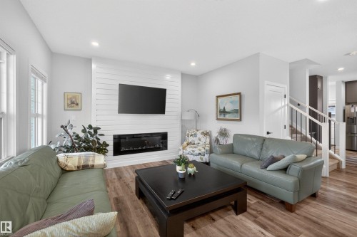 Living area featuring a shiplap accent wall with an integrated electric fireplace, wood-finish flooring, and recessed lighting - 53 Wingate Way, Fort Saskatchewan, AB - Indoor Photo Showing Living Room With Fireplace
