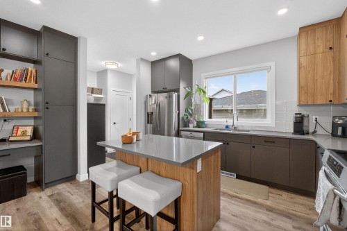 Modern kitchen featuring a central island with a light-toned countertop, wood-finish flooring, and recessed ceiling lighting - 53 Wingate Way, Fort Saskatchewan, AB - Indoor Photo Showing Kitchen