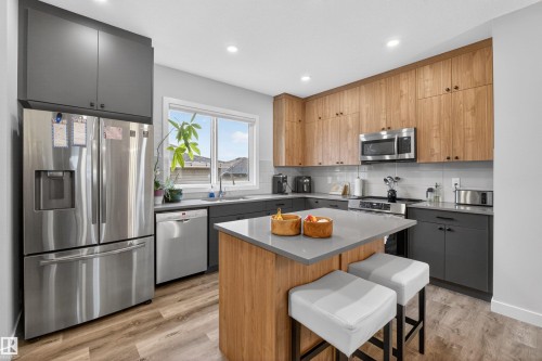 Modern kitchen featuring two-tone cabinetry, stainless steel appliances, wood-finish flooring, recessed lighting, and a kitchen island with seating - 53 Wingate Way, Fort Saskatchewan, AB - Indoor Photo Showing Kitchen