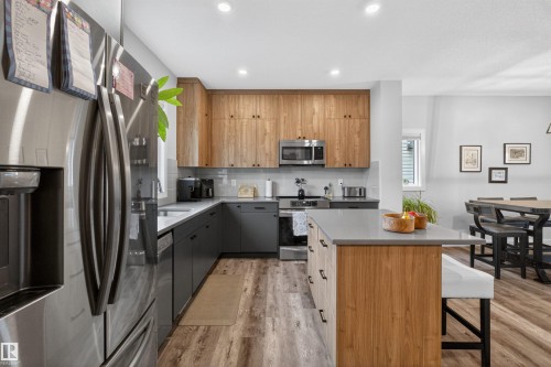 Contemporary kitchen featuring stainless steel appliances, two-tone cabinetry with wood-look upper cabinets and dark lower cabinets, a light-colored countertop, and recessed lighting - 53 Wingate Way, Fort Saskatchewan, AB - Indoor Photo Showing Kitchen