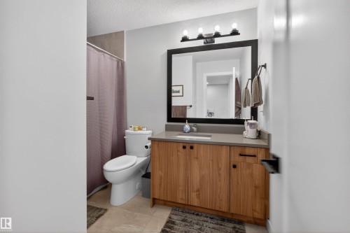 Bathroom featuring a wood-finish vanity with a light-colored countertop, an undermount sink, and a framed mirror with overhead lighting - 53 Wingate Way, Fort Saskatchewan, AB - Indoor Photo Showing Bathroom