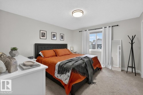 Carpeted bedroom featuring a window with white curtains, a flush-mount ceiling light, and light gray painted walls - 53 Wingate Way, Fort Saskatchewan, AB - Indoor Photo Showing Bedroom