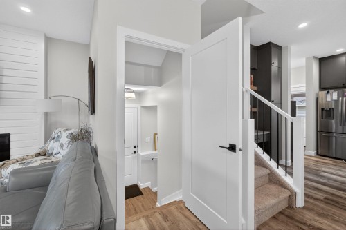 Interior entryway featuring a white paneled door with matte black hardware, carpeted stairs with white railing and black balusters, and wood-finish flooring - 53 Wingate Way, Fort Saskatchewan, AB - Indoor Photo Showing Other Room