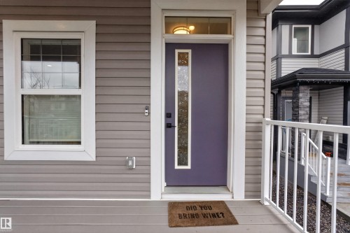 Gray horizontal siding exterior with a purple entry door featuring a vertical glass insert and a transom window above - 53 Wingate Way, Fort Saskatchewan, AB - Outdoor With Exterior