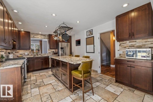 Spacious kitchen featuring extensive dark wood cabinetry, light granite countertops, a large center island with seating, stainless steel appliances, and large format tile flooring - 6003 176 Street, Edmonton, AB - Indoor Photo Showing Kitchen