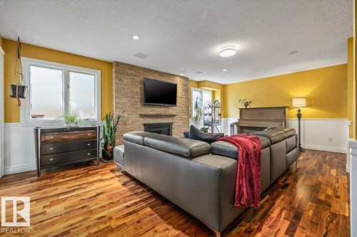 Spacious living area featuring wood-finish flooring, a stone-clad fireplace, and paneling with a contrasting paint scheme - 6003 176 Street, Edmonton, AB - Indoor Photo Showing Living Room With Fireplace
