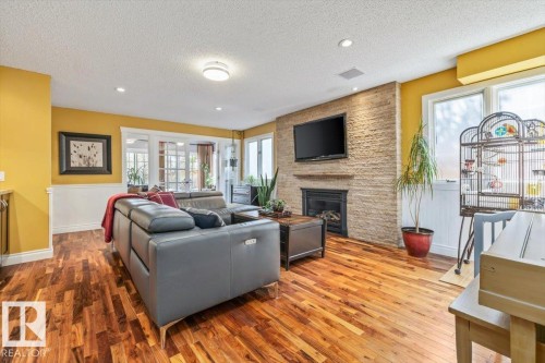 Living area featuring wood-finish flooring, a stone-clad fireplace with a mounted television, and white wainscoting - 6003 176 Street, Edmonton, AB - Indoor Photo Showing Living Room With Fireplace