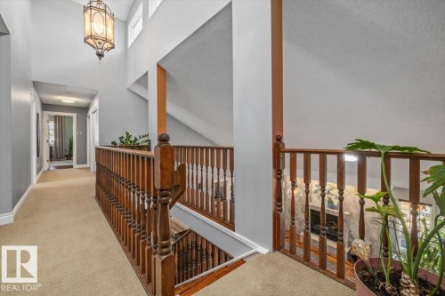 Upper-level hallway featuring a central wooden baluster, carpeted flooring, and a decorative pendant light fixture - 6003 176 Street, Edmonton, AB - Indoor Photo Showing Other Room