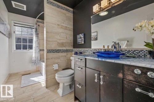Bathroom featuring a dark-toned vanity with decorative hardware, a blue vessel sink, and a large mirror with a multi-bulb light fixture - 6003 176 Street, Edmonton, AB - Indoor Photo Showing Bathroom