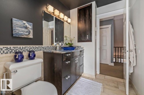 Bathroom featuring a dark wood-finish vanity with a light-toned countertop, a tile backsplash, and a contemporary light fixture above the mirror - 6003 176 Street, Edmonton, AB - Indoor Photo Showing Bathroom