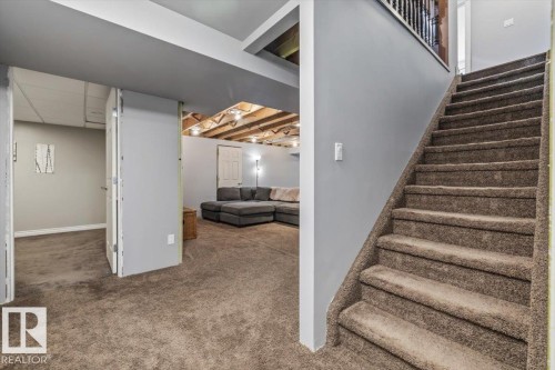 Carpeted staircase with an open balustrade leads to a lower level featuring gray walls, exposed ceiling joists, and a carpeted floor - 6003 176 Street, Edmonton, AB - Indoor Photo Showing Other Room
