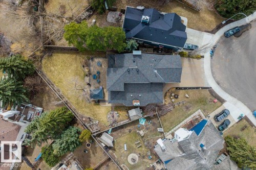 Shingled roofline over a multi-level dwelling, featuring a gravel driveway, a manicured lawn area, and mature evergreen trees - 6003 176 Street, Edmonton, AB - 