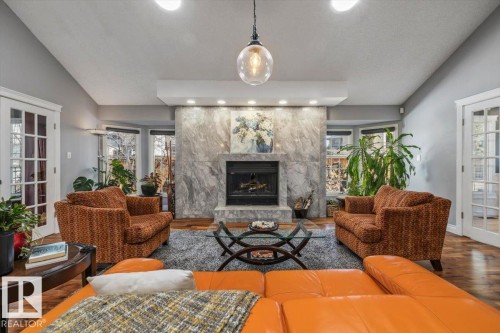 Living area featuring a stone-clad fireplace with a dark insert, bay windows, and wood-finish flooring - 6003 176 Street, Edmonton, AB - Indoor Photo Showing Living Room With Fireplace