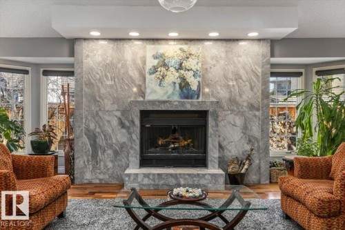 Central gas fireplace with a stone surround and hearth, flanked by bay windows - 6003 176 Street, Edmonton, AB - Indoor Photo Showing Living Room With Fireplace