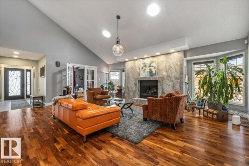 Spacious living area featuring rich wood-finish flooring, a vaulted ceiling, and a large fireplace with a stone surround - 6003 176 Street, Edmonton, AB - Indoor Photo Showing Living Room With Fireplace
