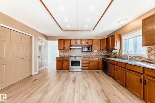 The kitchen features hardwood floors, light brown cabinetry, a tile backsplash, and a window above the sink - 4224 30 Street, Edmonton, AB - Indoor Photo Showing Kitchen With Double Sink