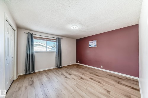 This room features light-toned wood flooring, a window with grey curtains, and a prominent accent wall in a deep purple hue - 4224 30 Street, Edmonton, AB - Indoor Photo Showing Other Room