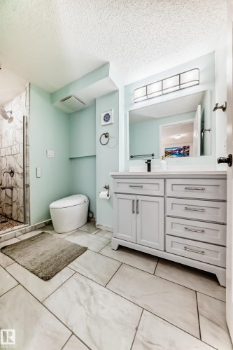 Well-appointed bathroom featuring a modern vanity with ample storage, a spacious shower with stone-tiled walls, and large format floor tiles - 4224 30 Street, Edmonton, AB - Indoor Photo Showing Bathroom