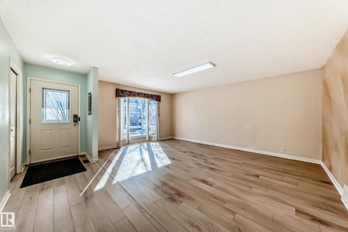 This property features light-colored wood flooring, a front door with a decorative glass panel, and large windows with natural light - 4224 30 Street, Edmonton, AB - Indoor Photo Showing Other Room