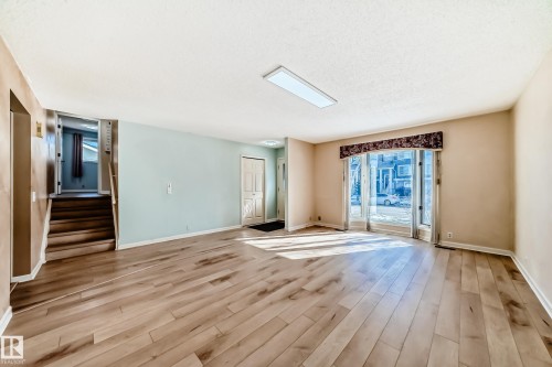 The property features light-colored wood flooring, a broad window with a valance, and a staircase with a wooden handrail - 4224 30 Street, Edmonton, AB - Indoor Photo Showing Other Room