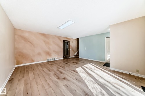 The spacious living area features light-toned hardwood flooring, a unique accent wall with a textured finish, and a rectangular ceiling light fixture - 4224 30 Street, Edmonton, AB - Indoor