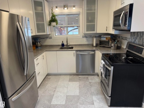 Modern kitchen featuring stainless steel appliances, white cabinetry with frosted glass accents, and a stone-finish countertop - 11948 132 Street, Edmonton, AB - Indoor Photo Showing Kitchen