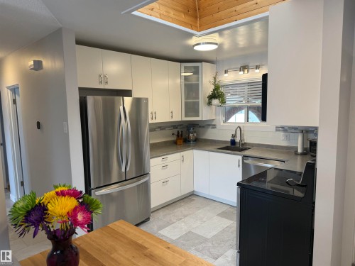 Kitchen featuring white cabinetry, stainless steel appliances, a tile backsplash, light-toned countertops, and a wood-paneled ceiling element - 11948 132 Street, Edmonton, AB - Indoor Photo Showing Kitchen