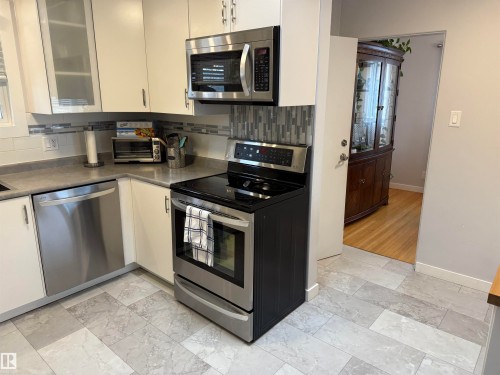 Kitchen featuring stainless steel appliances, white cabinetry, a mosaic tile backsplash, and light-toned, variegated tile flooring - 11948 132 Street, Edmonton, AB - Indoor Photo Showing Kitchen