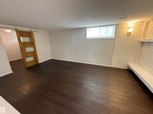 Spacious room featuring dark wood-finish flooring, white painted brick accent wall, built-in bench seating, and a sliding barn door with frosted glass panels - 11948 132 Street, Edmonton, AB - Indoor Photo Showing Other Room