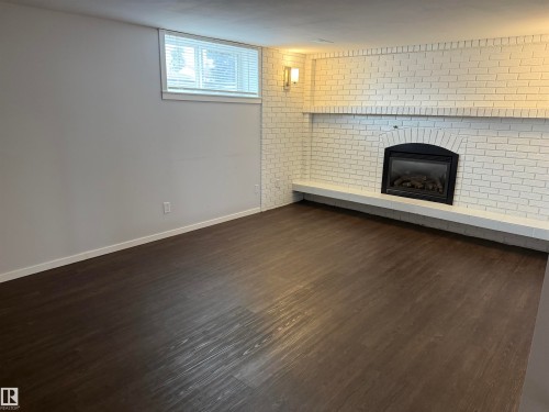 Spacious room featuring dark wood-finish flooring, light gray walls, and a white painted brick fireplace with a black insert - 11948 132 Street, Edmonton, AB - Indoor With Fireplace