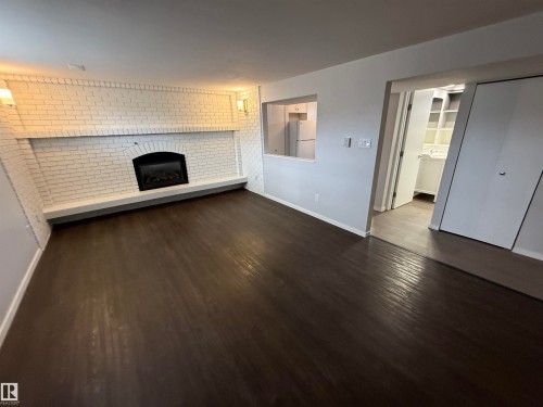 Spacious living area featuring dark wood-finish flooring, a white-painted brick fireplace with an electric insert, and a wide hearth - 11948 132 Street, Edmonton, AB - Indoor Photo Showing Living Room With Fireplace